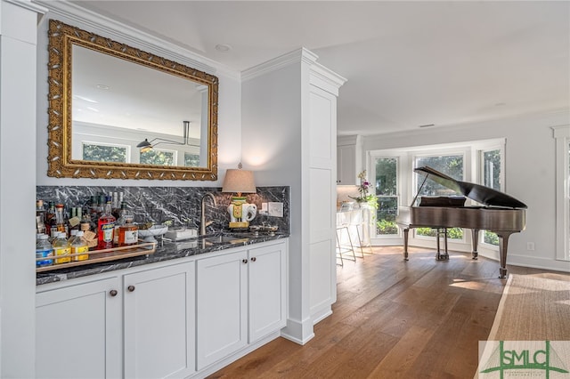 bar featuring backsplash, dark wood-type flooring, ornamental molding, a sink, and wet bar