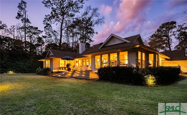 back of house at dusk featuring a lawn and a chimney