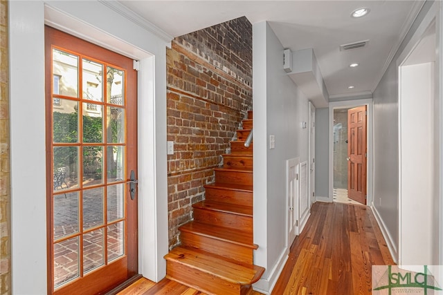 stairs featuring crown molding, brick wall, and hardwood / wood-style floors