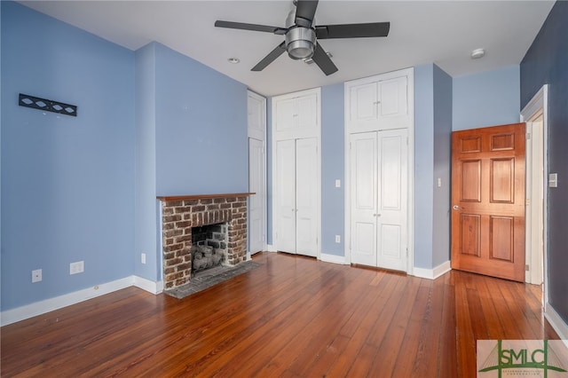 unfurnished living room with a brick fireplace, dark wood-type flooring, and ceiling fan