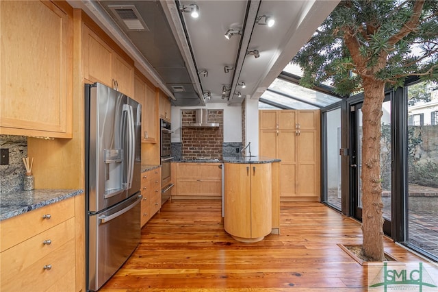 kitchen with stainless steel appliances, light hardwood / wood-style floors, a kitchen island, and dark stone countertops