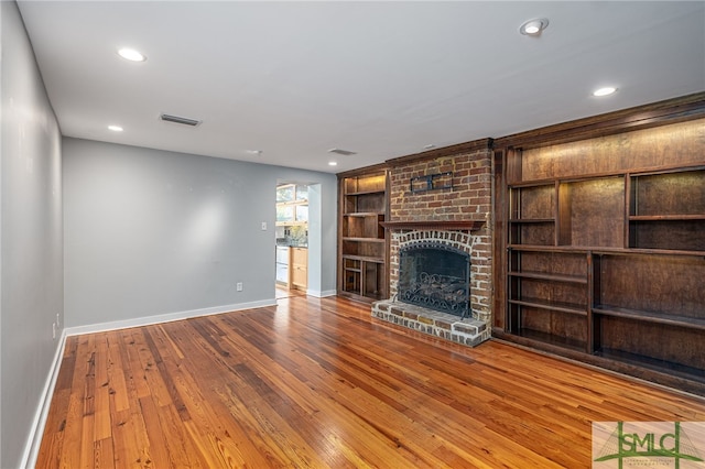 unfurnished living room featuring built in shelves, hardwood / wood-style floors, and a brick fireplace