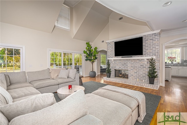 living room featuring light hardwood / wood-style flooring, crown molding, a fireplace, and high vaulted ceiling