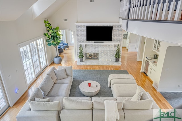 living room with high vaulted ceiling, a brick fireplace, and light wood-type flooring