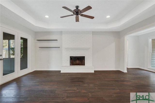 unfurnished living room with dark hardwood / wood-style flooring, a brick fireplace, and a tray ceiling