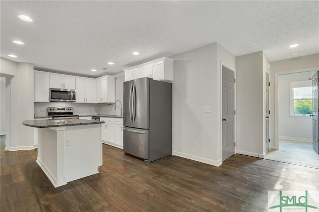 kitchen featuring a kitchen island, white cabinetry, dark hardwood / wood-style flooring, dark stone counters, and stainless steel appliances