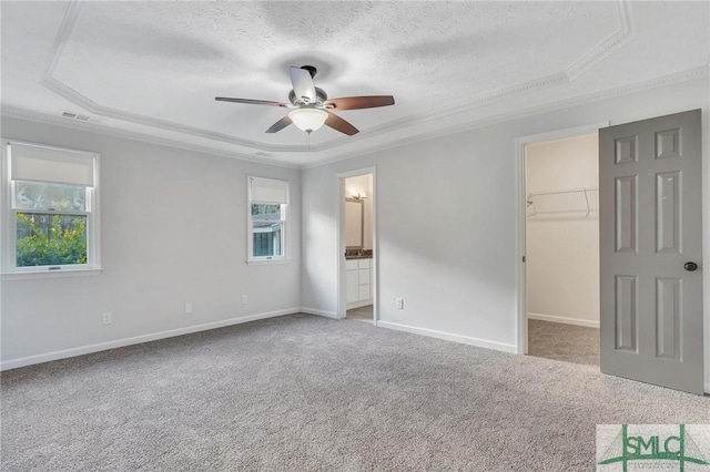 unfurnished bedroom with crown molding, a spacious closet, a textured ceiling, a tray ceiling, and carpet