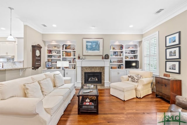 living room with hardwood / wood-style floors, built in shelves, a fireplace, and ornamental molding