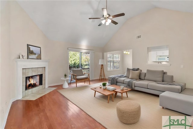 living room featuring a tile fireplace, high vaulted ceiling, ceiling fan, and light wood-type flooring