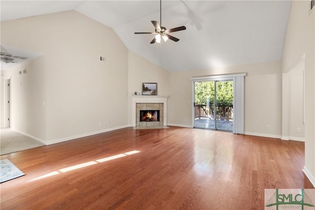 unfurnished living room with ceiling fan, wood-type flooring, a tiled fireplace, and high vaulted ceiling