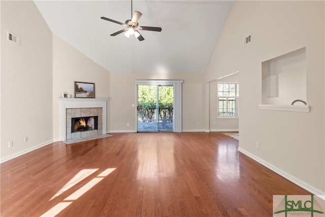 unfurnished living room with hardwood / wood-style flooring, ceiling fan, a tiled fireplace, and high vaulted ceiling