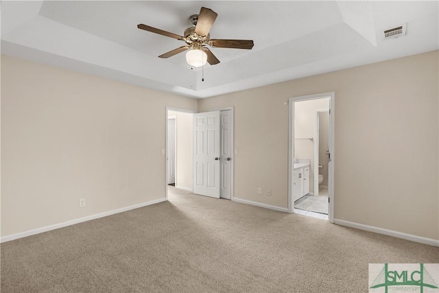 unfurnished bedroom with connected bathroom, light colored carpet, and a raised ceiling