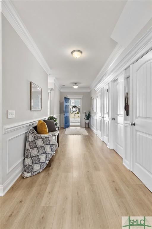 corridor with ornamental molding, a wainscoted wall, a decorative wall, and light wood finished floors