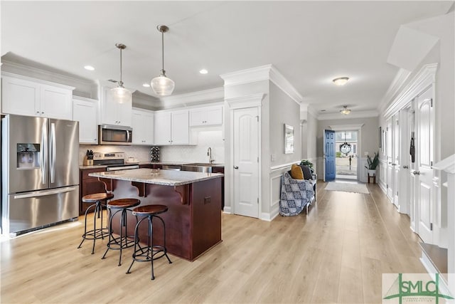 kitchen with light stone counters, a breakfast bar, hanging light fixtures, appliances with stainless steel finishes, and a kitchen island