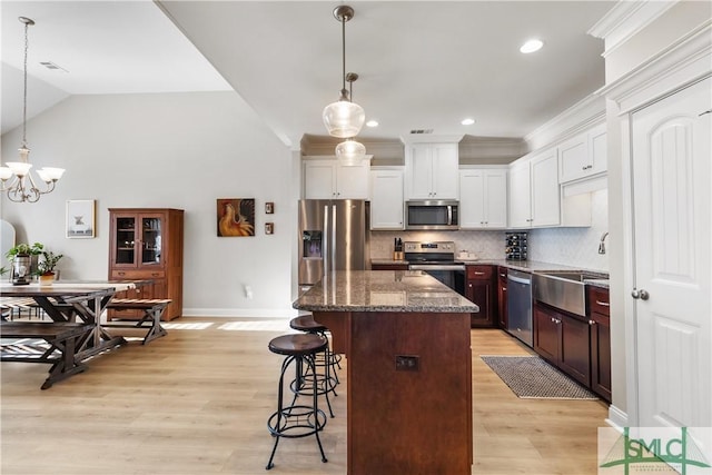 kitchen featuring a sink, white cabinetry, hanging light fixtures, appliances with stainless steel finishes, and a kitchen bar