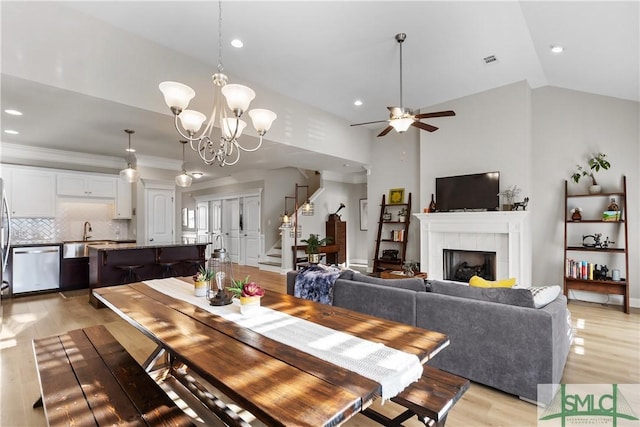 dining area featuring lofted ceiling, light wood-style flooring, visible vents, stairway, and a tiled fireplace