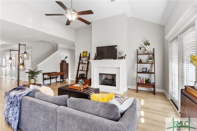 living area featuring a fireplace, lofted ceiling, ceiling fan, light wood-type flooring, and stairs