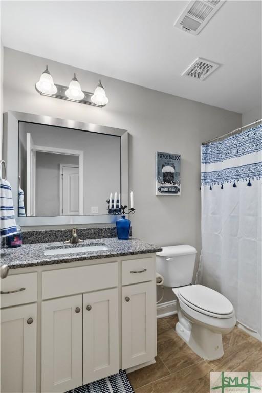 full bathroom featuring toilet, vanity, visible vents, and baseboards