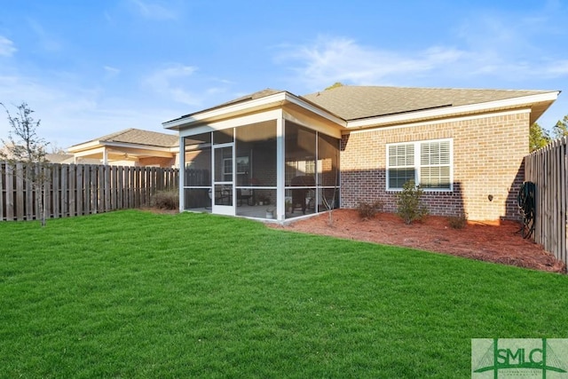 rear view of house featuring a yard, brick siding, a fenced backyard, and a sunroom