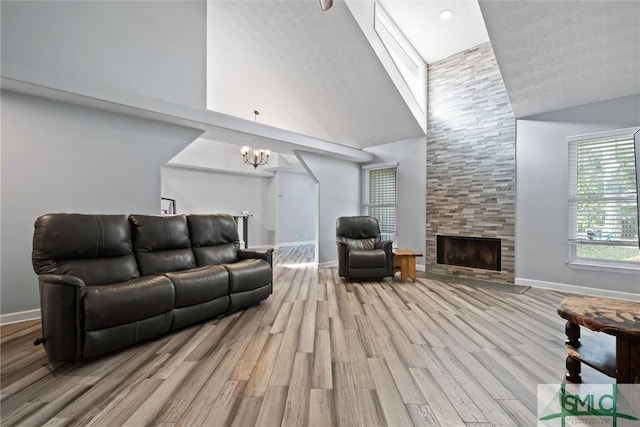 living room with a towering ceiling, an inviting chandelier, a fireplace, light hardwood / wood-style floors, and a textured ceiling