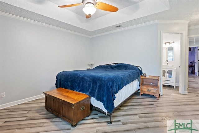 bedroom with crown molding, light hardwood / wood-style flooring, ensuite bathroom, a tray ceiling, and a textured ceiling