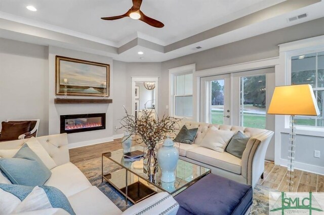 living room with ceiling fan, a tray ceiling, light wood-type flooring, and french doors