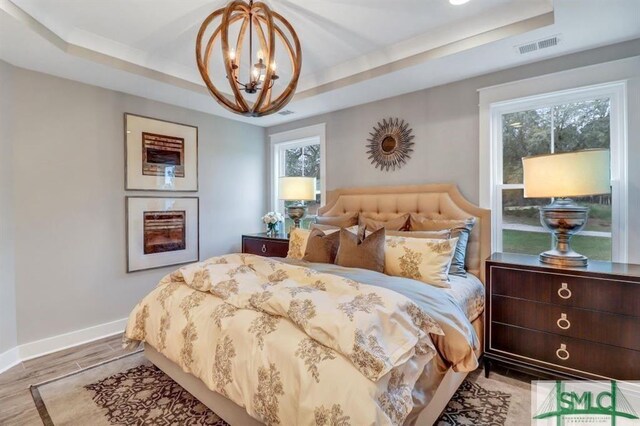 bedroom with a raised ceiling, light hardwood / wood-style flooring, and a notable chandelier