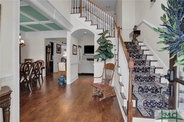 stairway with crown molding, a towering ceiling, wood-type flooring, and a notable chandelier