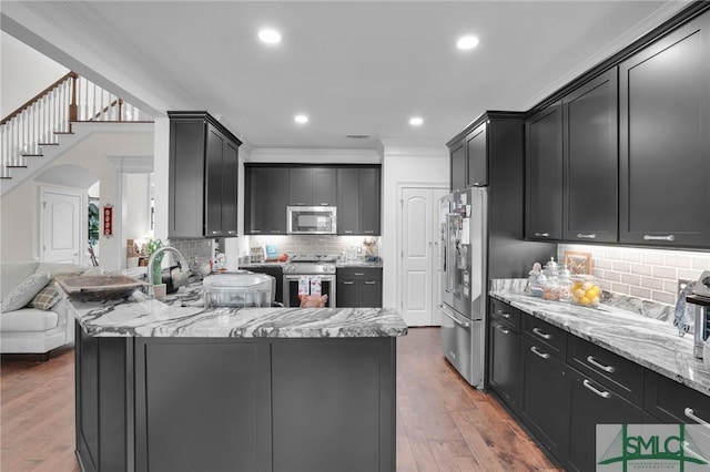 kitchen with ornamental molding, appliances with stainless steel finishes, light stone countertops, light hardwood / wood-style floors, and backsplash