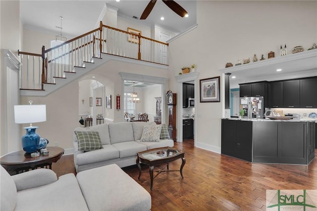 living room with crown molding, ceiling fan with notable chandelier, dark hardwood / wood-style floors, and a towering ceiling