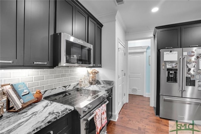 kitchen featuring crown molding, appliances with stainless steel finishes, dark hardwood / wood-style floors, light stone countertops, and decorative backsplash