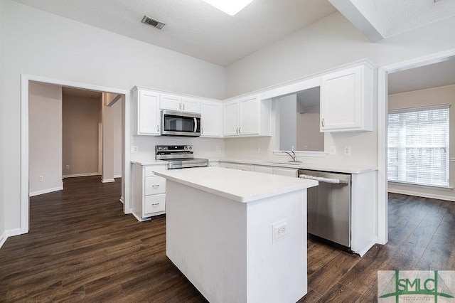 kitchen with sink, appliances with stainless steel finishes, white cabinets, a kitchen island, and dark hardwood / wood-style flooring