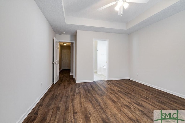 unfurnished bedroom with a raised ceiling, dark wood-type flooring, connected bathroom, and ceiling fan