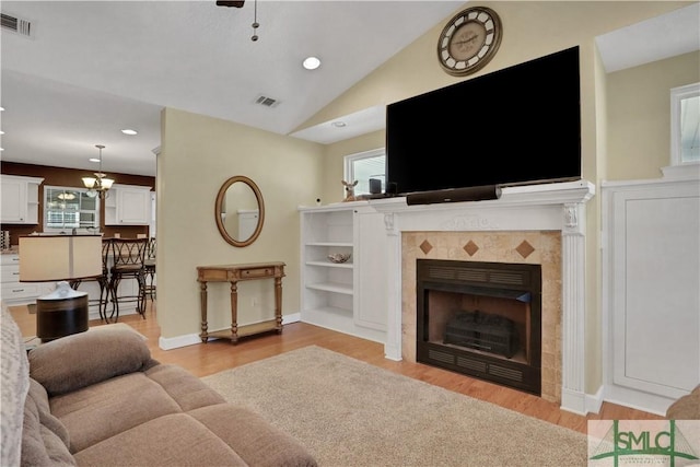 living room with a tile fireplace, lofted ceiling, plenty of natural light, and light hardwood / wood-style flooring