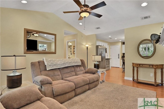 living room with ceiling fan, vaulted ceiling, and light wood-type flooring