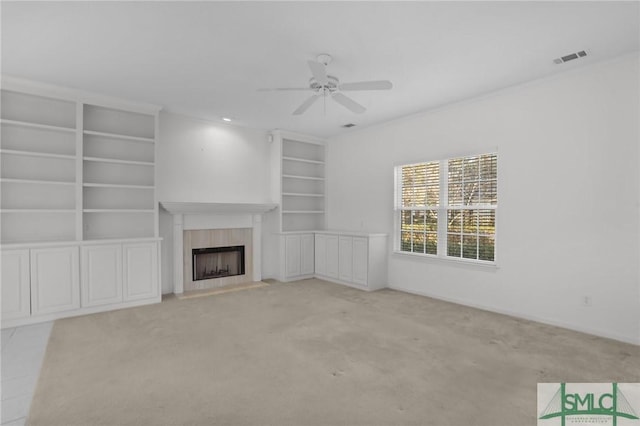 unfurnished living room featuring crown molding, built in features, ceiling fan, a fireplace, and light carpet