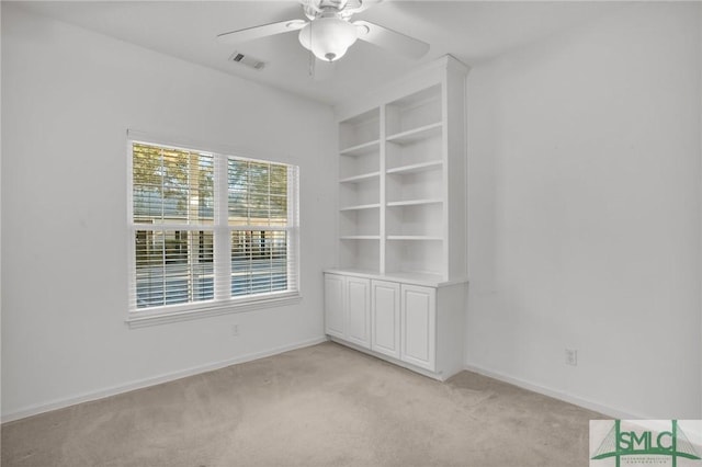 spare room with built in shelves, ceiling fan, and light carpet