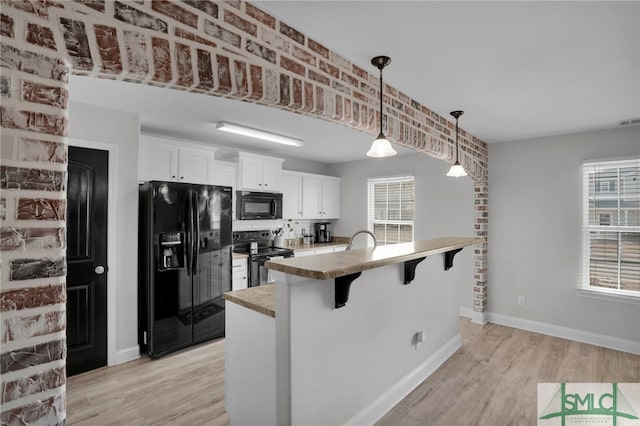 kitchen with a breakfast bar area, hanging light fixtures, black appliances, white cabinets, and light wood-type flooring