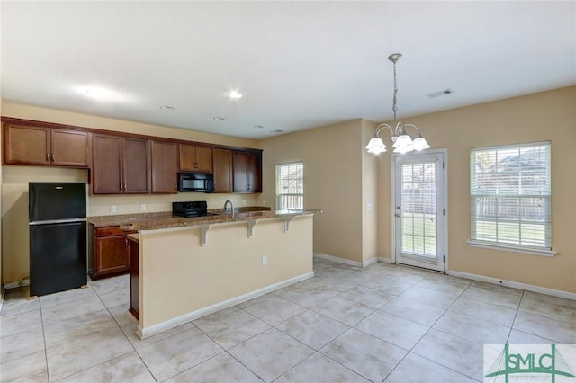 kitchen with a breakfast bar, light tile patterned floors, pendant lighting, light stone countertops, and black appliances