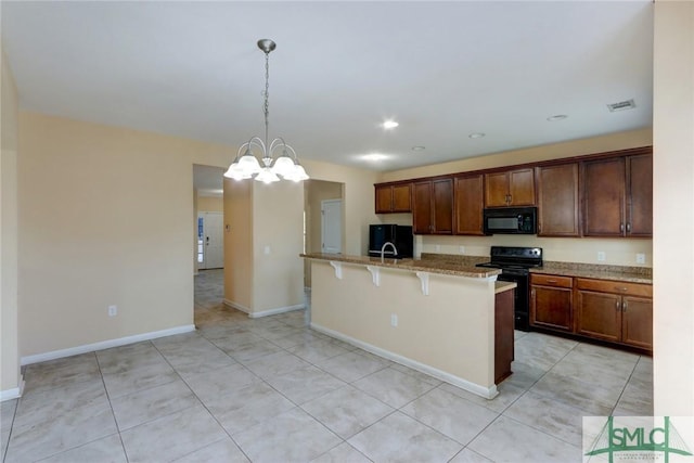 kitchen featuring pendant lighting, a breakfast bar area, black appliances, light stone countertops, and a center island with sink