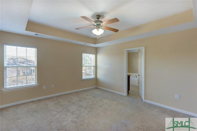 empty room with light carpet, a tray ceiling, and ceiling fan