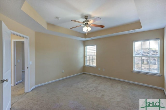 carpeted empty room featuring ceiling fan and a raised ceiling