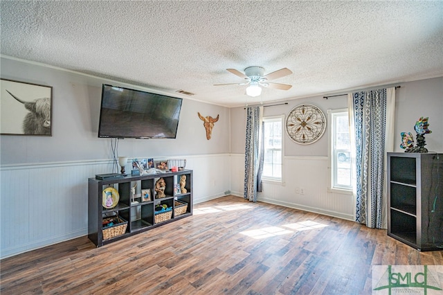 living room with ceiling fan, hardwood / wood-style flooring, ornamental molding, and a textured ceiling