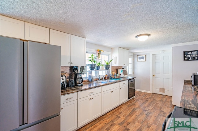 kitchen with sink, light hardwood / wood-style flooring, stainless steel refrigerator, white cabinetry, and tasteful backsplash