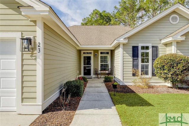 entrance to property featuring an attached garage, a shingled roof, a porch, and a lawn