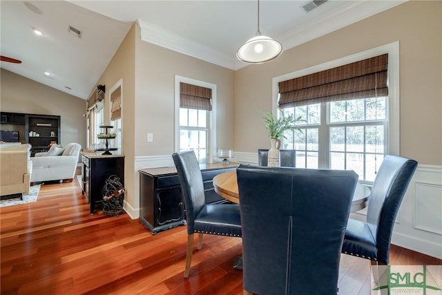 dining space with a wainscoted wall, vaulted ceiling, wood finished floors, and a decorative wall