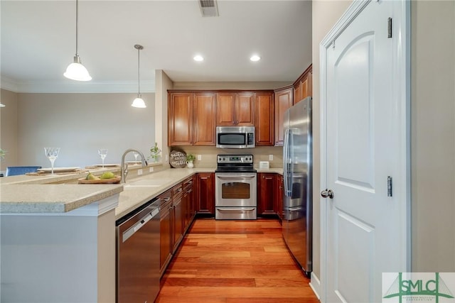 kitchen featuring decorative light fixtures, sink, kitchen peninsula, stainless steel appliances, and light wood-type flooring