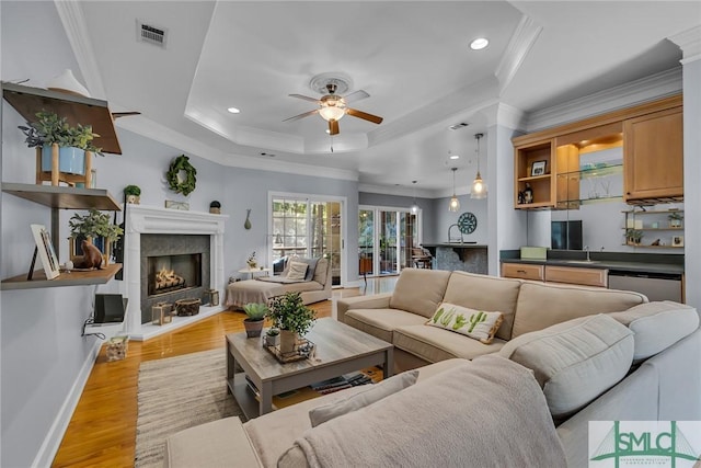 living room with sink, ornamental molding, a raised ceiling, ceiling fan, and light hardwood / wood-style floors