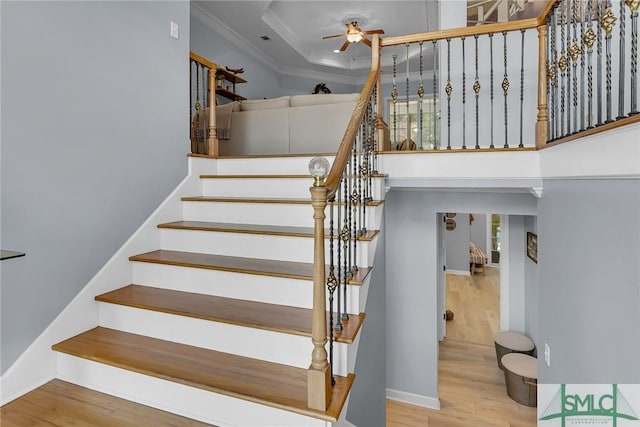 stairs with ceiling fan, ornamental molding, a tray ceiling, and wood-type flooring