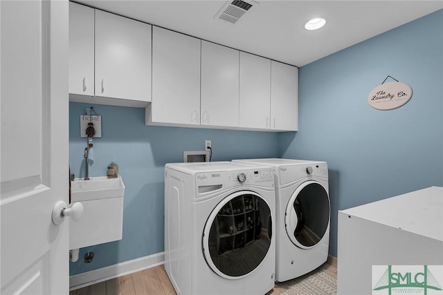 clothes washing area with cabinets, washer and dryer, sink, and light hardwood / wood-style flooring